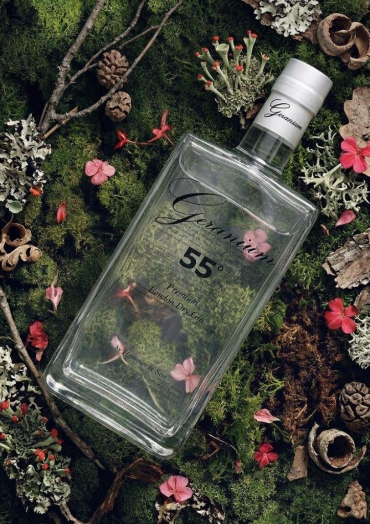 Geranium Gin 55° Navy Strength bottle on a forest bed of moss, pinecones, and geranium flowers.